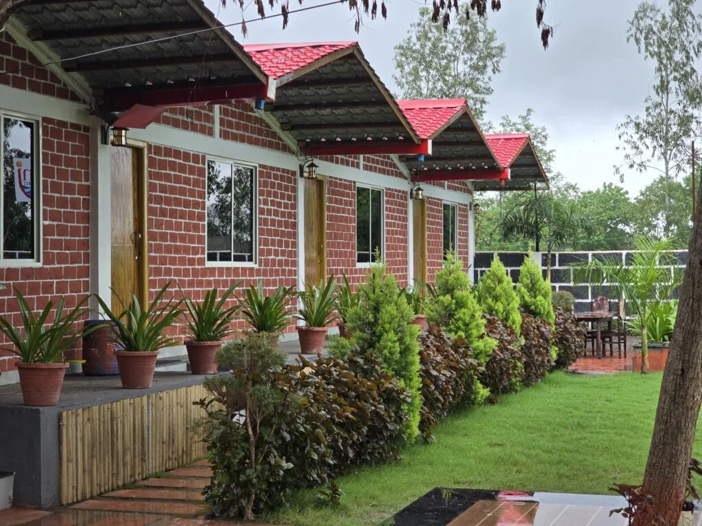 Brick cottages beside a green lawn and planted walkway at Kunj Resort